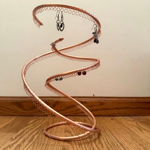 May include: A copper wire earring holder in the shape of a spiral. The holder has multiple loops for hanging earrings. There are several pairs of earrings hanging on the holder.