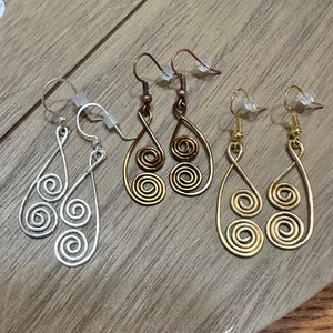 May include: Three pairs of dangle earrings with a spiral design. The earrings are silver, gold, and bronze.