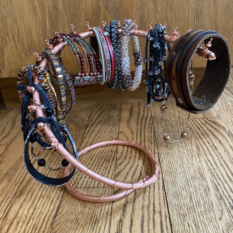 May include: A copper wire jewelry stand with a variety of bracelets and necklaces. The stand is shaped like a spiral and has a round base. The jewelry is made of different materials, including leather, beads, and metal.