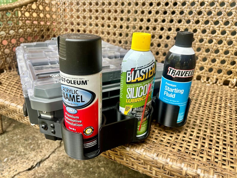 Peut inclure: Un support en plastique noir &agrave; trois emplacements pour bombes a&eacute;rosols fix&eacute; sur une mallette de rangement grise. Le support contient une bombe de peinture &eacute;mail acrylique Rust-Oleum, un lubrifiant silicone Blaster et un fluide de d&eacute;marrage.