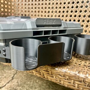 Peut inclure: Un organisateur de rangement en plastique gris avec un couvercle transparent et le mot FLEX en relief sur le loquet avant. Trois porte-gobelets cylindriques noirs &agrave; fa&ccedil;ade ouverte sont fix&eacute;s &agrave; l'avant par des vis m&eacute;talliques.