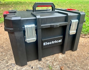 Peut inclure: Une boîte à outils en plastique noir dotée d'une poignée de transport supérieure avec des accents rouges, de deux loquets métalliques argentés sur le devant et d'une étiquette noire rectangulaire avec le texte blanc Electrical sur le panneau avant.
