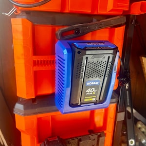 May include: A blue and black Kobalt 40V MAX extended run lithium-ion battery pack. The battery is mounted on an orange tool storage box. A black handle is above the battery.