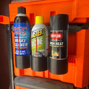 May include: An orange tool organizer with three cans of automotive products. The cans are labeled "Shop Pro Brake Cleaner", "Blaster Silicone Lubricant", and "Krylon High Heat" spray paint. The organizer is mounted on a dark surface.
