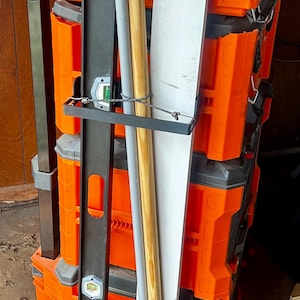 May include: An orange and black rolling tool storage system with a variety of tools. The system includes a level, a wooden handled tool, and a white board. The system has a wheel for easy transport.