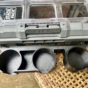 Peut inclure: Un organisateur de rangement Flex Stack Pack en plastique gris et transparent avec une poign&eacute;e sup&eacute;rieure et plusieurs compartiments, fix&eacute; &agrave; un support d'accessoires en plastique noir avec trois porte-gobelets circulaires &agrave; l'avant.