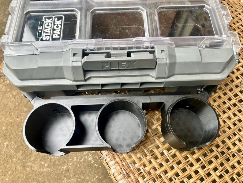 Peut inclure: Un organisateur de rangement Flex Stack Pack en plastique gris et transparent avec une poign&eacute;e sup&eacute;rieure et plusieurs compartiments, fix&eacute; &agrave; un support d'accessoires en plastique noir avec trois porte-gobelets circulaires &agrave; l'avant.
