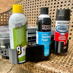 Peut inclure: Un support de rangement en plastique noir dot&eacute; de trois compartiments circulaires, contenant chacun une bombe a&eacute;rosol diff&eacute;rente. Les bombes incluent un produit de marque Blaster &agrave; capuchon jaune, un fluide de d&eacute;marrage Traveler et une peinture Rust-Oleum.