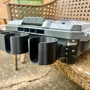 Peut inclure: Une mallette de rangement en plastique gris et noir avec le mot FLEX en relief sur la poign&eacute;e. Deux porte-gobelets cylindriques noirs avec des fentes lat&eacute;rales ouvertes sont fix&eacute;s &agrave; l'avant par un support noir avec des vis visibles.