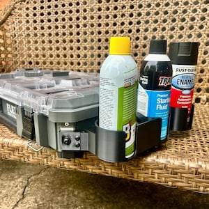 Peut inclure: Une mallette &agrave; outils en plastique gris avec un couvercle transparent et un support lat&eacute;ral noir imprim&eacute; en 3D contenant trois bombes a&eacute;rosols. Les bombes incluent un spray &agrave; bouchon jaune, un fluide de d&eacute;marrage bleu et un spray &eacute;mail noir.
