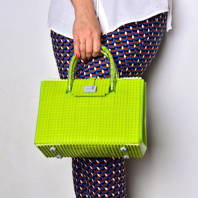 Peut inclure: Un sac &agrave; main vert vif compos&eacute; de pi&egrave;ces en plastique qui s'embo&icirc;tent, ressemblant &agrave; des briques Lego. Le sac a un fermoir argent&eacute; et une poign&eacute;e en plastique transparent.