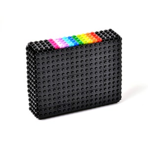 May include: A rectangular black clutch made of interlocking toy blocks. The top edge features a rainbow gradient of colorful blocks. The clutch is a unique accessory, perfect for carrying essentials.