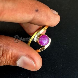 May include: A gold ring with a pink gemstone set in the center. The ring is designed with a twisted band.