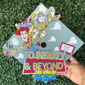 Puede incluir: Un birrete de graduación decorado con personajes de Toy Story. Se representan a Buzz Lightyear y Woody, con la frase "To Infinity & Beyond". También se muestra el año "2025". El birrete es azul claro con nubes blancas.
