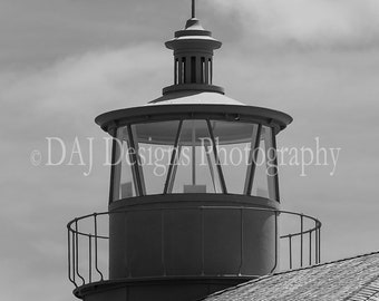 May include: Black and white photo of a lighthouse with a metal roof and a glass lantern room. The lighthouse is against a cloudy sky.