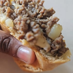 Peut inclure: Gros plan sur une main tenant une pâtisserie à moitié mangée remplie de viande hachée et de fromage.