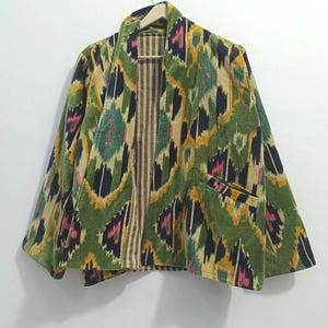 Può includere: Giacca fantasia con un design verde, giallo, rosa e blu navy. La giacca ha un colletto, due tasche e un interno a righe. La giacca è appesa a una gruccia di legno.