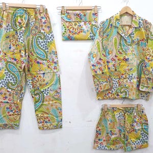 May include: A four-piece pajama set with a vibrant paisley pattern in yellow, green, blue, and red. The set includes long pants, a button-down shirt, shorts, and a small pouch, all hanging on wooden hangers.