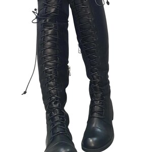 May include: Black, knee-high boots with a lace-up design. The boots have a rounded toe and a zipper on the side. The laces extend up the front of the boots. The boots are made of a smooth, leather-like material.