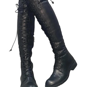 May include: Black leather knee-high boots with lace-up detailing. The boots have a rounded toe and a low heel. The laces extend up the front of the boots. The boots are made of a smooth, matte leather.
