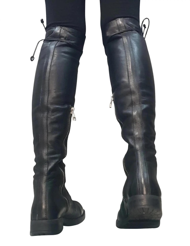 May include: Black leather over-the-knee boots with silver zippers and laces at the top. The boots have a flat sole and are designed to be worn over the knee. The boots are made of a smooth, shiny leather material.