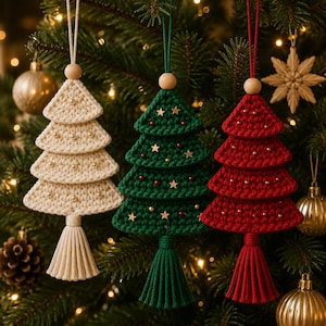 Op de afbeelding: Drie gelaagde gehaakte kerstboomhangers in crème, donkergroen en rood. Elke boom heeft een houten kraal aan de bovenkant, een bijpassend kwastje aan de onderkant en is versierd met kleine parels, gouden sterren en rode kraaltjes.