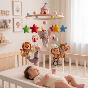 May include: A circus-themed nursery mobile featuring felt plush animals including a lion, elephant, monkey, bear, and seal. The mobile includes colorful stars, popcorn buckets, and a central tent structure suspended from a circular wooden frame.
