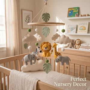 Op de afbeelding: Een hangende babymobiel met vilten safaridieren, waaronder een leeuw, zebra, olifant, giraf en neushoorn. De mobiel bevat beige wolken, groene vilten bladeren en witte en groene vilten ballen die aan een rond houten frame zijn bevestigd.