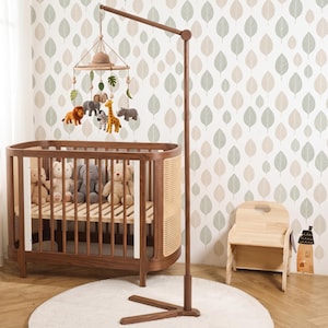 Könnte beinhalten: Ein Holzkinderbett mit Seitenteilen aus Wiener Geflecht, ein hoher Holzständer und ein hängendes Mobile mit Plüsch-Safari-Tieren wie Löwe, Elefant, Zebra, Giraffe und Nashorn. Im Kinderbett befinden sich vier Plüschtiere und Elefantenfiguren.