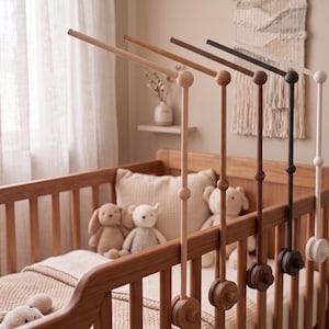 May include: A set of four wooden crib mobile arms in varying shades of light wood, medium brown, dark brown, and white. Each arm features a vertical post with a circular knob, a horizontal extension, and a circular mounting clamp at the base.
