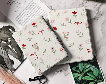 May include: Two white Kindle e-reader cases with a floral pattern. The pattern features red, pink, and green flowers, leaves, and bows. The cases are made of a soft, textured material.