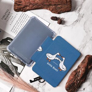 May include: A clear, protective case and two blue Goose Bumps-themed covers. The covers feature white geese with orange feet and beaks, and the text "Goose Bumps". The items are on a marble surface.