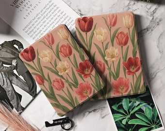 May include: Two rectangular notebooks with a floral tulip design in red, peach, and cream colors on a light pink background. The notebooks are placed on a marble surface, with a book and a small black bottle opener nearby.