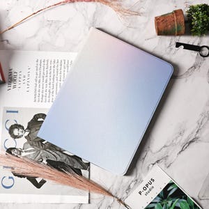 May include: A light blue and pink ombre notebook cover with a textured surface. The cover is blank and has a subtle shimmer.