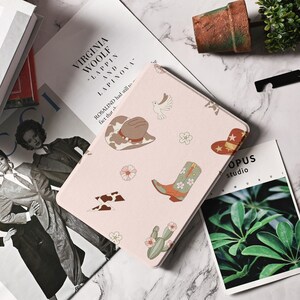 May include: A pink and white iPad case with a western theme. The case features a cowboy hat, boots, lightning bolts, and cacti. The text "ROSALIND had still to face that..." is printed on the case.