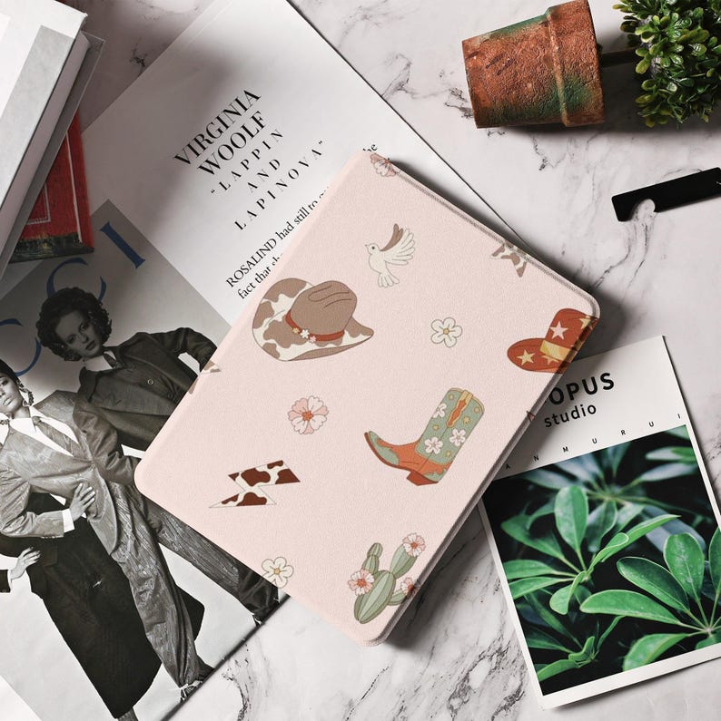 May include: A pink and white iPad case with a western theme. The case features a cowboy hat, boots, lightning bolts, and cacti. The text "ROSALIND had still to face that..." is printed on the case.