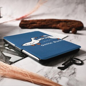 May include: A blue tablet case featuring a cartoon illustration of two white geese with orange feet and the words "Goose Bumps." A black bottle opener keychain with a Spotify code is also visible.