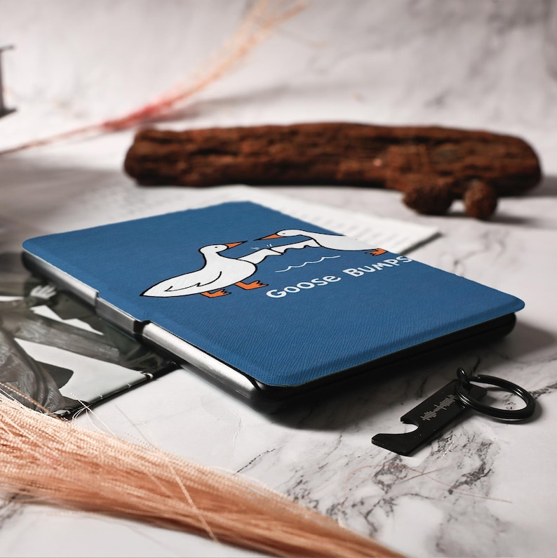 May include: A blue tablet case featuring a cartoon illustration of two white geese with orange feet and the words "Goose Bumps." A black bottle opener keychain with a Spotify code is also visible.