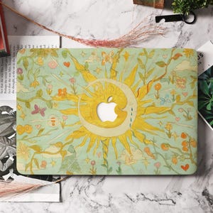 May include: A laptop case with a whimsical design featuring a sun, moon, and apple logo cutout. The case has a light green background with floral and butterfly illustrations in yellow, orange, and pink. The sun and moon are yellow.