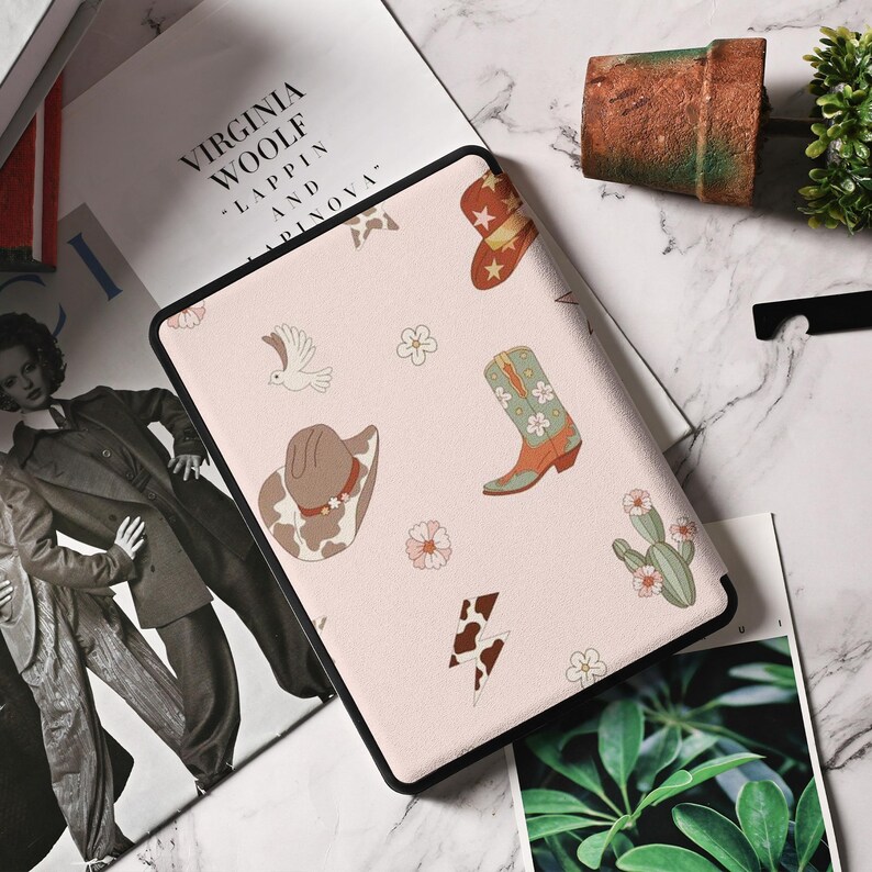 May include: A pink e-reader case with a black border. The case has a repeating pattern of cowboy boots, hats, and flowers.