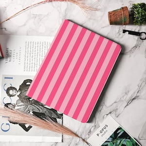 May include: A pink and light pink striped tablet case. The case is rectangular with rounded corners. The stripes are vertical and evenly spaced. The case is on a marble surface.