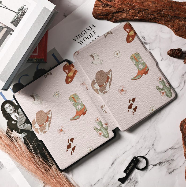 May include: A pink and white e-reader case with a cowboy boot, hat, and cactus pattern. The case has the text "Virginia Woolf" printed on the front.