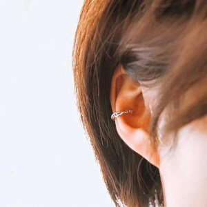 May include: A silver ear cuff with a delicate, intricate design. The cuff is worn on the upper part of the ear, just above the lobe.
