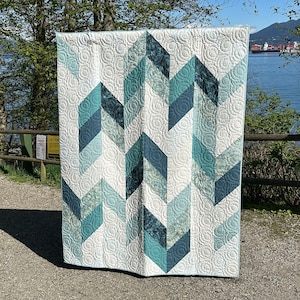 Op de afbeelding: Een quilt met een geometrisch patroon in tinten blauw en wit. De quilt is gemaakt van verschillende stoffen en heeft een gestikt ontwerp.