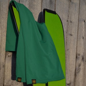 Puede incluir: Un par de esquís verdes con una funda a juego, contra una pared de madera envejecida. Los esquís tienen una base verde brillante y detalles en negro. La funda es de un verde más oscuro y tiene un pequeño parche con un logotipo. Los esquís miden unos 170 cm.
