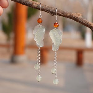 May include: A pair of silver dangle earrings with a jade fish charm and three white beads on each earring.