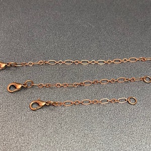 May include: Three gold-toned chain extenders of different lengths. Each extender has a lobster clasp on one end and a jump ring on the other.
