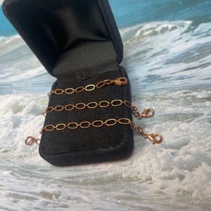 May include: A gold chain necklace in a black velvet box. The chain is made of oval links and has a lobster clasp.