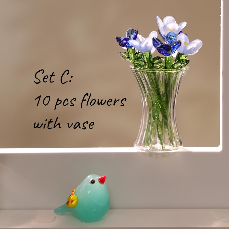 May include: A glass vase with 10 glass flowers in shades of blue and white. A small, turquoise glass bird with a red beak and yellow accents sits below. The text "Set C: 10 pcs flowers with vase" is visible.