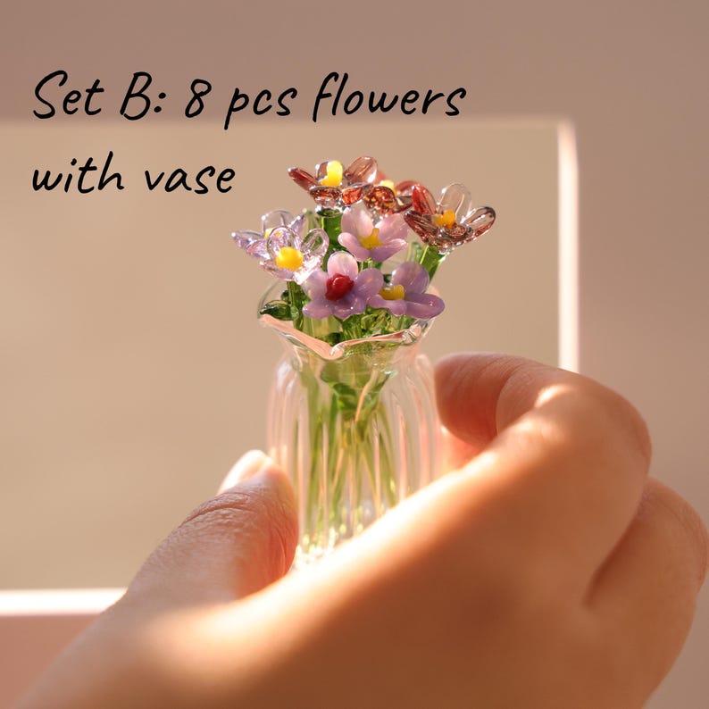 May include: A miniature glass vase filled with eight glass flowers in shades of purple, pink, and yellow. The text "Set B: 8 pcs flowers with vase" is visible. The vase is held in a person's hand.